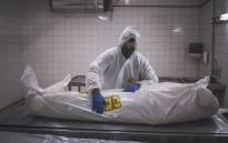 A morgue attendant at the Pretoria branch of Avbob applies a biohazard warning on the body of a patient deceased of COVID-19 related illnesses. Picture: AFP