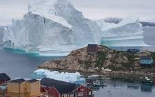 This picture was taken on 13 July 2018 shows an iceberg behind houses and buildings after it grounded outside the village of Innarsuit, an island settlement in the Avannaata municipality in northwestern Greenland. Picture: AFP.