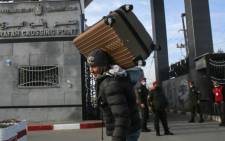 A man carries a suitcase on his shoulder while members of the Palestinian security forces loyal to Hamas, mask-clad due to the coronavirus pandemic, stand guard at the Rafah border crossing with Egypt, in the southern Gaza Strip, on 9 February 2021, which reopened after an Egyptian announcement to let through incoming traffic until further notice. Picture: SAID KHATIB/AFP