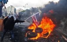 A Palestinian protester sets alight an America flag during clashes with Israeli troops at a protest against US President Donald Trump's decision to recognize Jerusalem as the capital of Israel, near the Jewish settlement of Beit El, near the West Bank city of Ramallah on 7 December 2017. Picture: AFP.