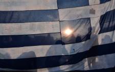 Protestors stand behind a huge Greek flag in front of the Greek parliament in central Athens, on 29 June 2015. Picture: AFP.