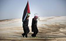 A man holding a Palestinian flag and a woman carrying an olive tree, walk through rows of greenhouses on "Land Day" during which people notably plant olive trees on 29 March, 2014 near the Israeli border in Jabalia, in the northern Gaza Strip. Picture: AFP.