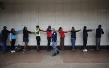 A member of the South African Police Service (SAPS) enforces social distancing as he makes shoppers hold their hands out in front of them to ensure that they are at least one metre apart from one another while they queue outside a supermarket in Yeoville, Johannesburg, on 28 March 2020. Picture: AFP