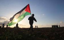 FILE: A Palestinian protester carries a national flag during a demonstration near the border between Israel and Khan Yunis in the southern Gaza Strip, on 21 December 2018. A 16-year-old Palestinian was killed today by Israeli fire during border protests and clashes east of Gaza City, the health ministry in the Hamas-run enclave said. Picture: AFP.