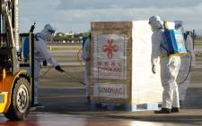 This handout photo taken on February 28, 2021 and received from the Presidential Communications Operations Office (PCOO) shows workers in protective suits disinfecting one of the crates containing the first batch of Sinovac vaccines shortly after its arrival onboard a Chinese air force plane at Villamor air base in Manila. Picture: Presidential Communications Operations Office / AFP