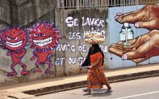 A woman walks past graffiti on a wall depicting hygiene measures to curb the spread of the COVID-19 coronavirus in Conakry, Guinea, on 4 May 2020. Picture: AFP

