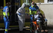 FILE: Healthcare workers wearing protective suits push a man on a wheelchair outside the 12 Octubre Hospital in Madrid on 2 April 2020. Picture: AFP