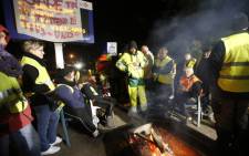 Yellow vest protesters listen near a loudspeaker and a banner reading "everybody together" on A9 road near Le Boulou, southern France on 10 December, 2018 as French president delivers a TV speech following the so-called "yellow jacket crisis". Picture: AFP