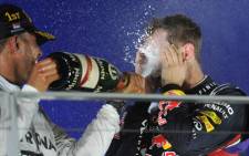Mercedes driver Lewis Hamilton of Britain (L) sprays the bottle of champagne over Red Bull Racing driver Sebastian Vettel of Germany (R) on the podium after winning the Formula One Singapore Grand Prix at the Marina Bay street circuit on 21 September, 2014. Picture: AFP.