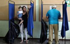 A boy holds his mothers vote as she exits a polling booth during the Greek referendum in Thessaloniki on 5 July, 2015. Greek voters headed to the polls today to vote in a historic, tightly fought referendum on whether to accept worsening austerity in exchange for more bailout funds, in a gamble that could see it crash out of the euro. Picture: AFP.
