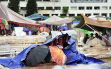 Pakistani supporters of Canadian cleric Tahir ul Qadri take cover under plastic sheeting during heavy rain on the lawn of the Parliament premises during an anti-government protest in Islamabad on 4 September 2014. Picture: AFP.
