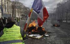 A Yellow Vest protester waves a French national flag while standing behind a burning barricade on the Champs-Elysees in Paris on 16 March 2019, during the 18th consecutive Saturday of demonstrations called by the 'Yellow Vest' (gilets jaunes) movement. Picture: AFP