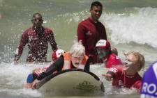 Pamela Hanford (75) is helped by a team of coaches and volunteers to surf at an adaptive surfing event at Muizenberg beach, on 20 January 2019, in Cape Town, South Africa. Picture: AFP