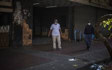 A plain clothed South African policeman carries a whip while he and an uniformed colleague try to clear a pavement in Hillbrow, Johannesburg, on 27 March 2020 in an effort to enforce distancing. Picture: AFP