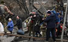 A woman carries a dog while people cross a destroyed bridge as they evacuate the city of Irpin during heavy shelling and bombing on 5 March 2022. Picture: Aris Messinis/AFP