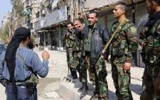 FILE: Pro-regime fighters speak with a rebel fighter in the town of Babbila, a suburb of Damascus, during a cease fire agreement between the group controlling the town and the regime on 17 February, 2014. Picture: AFP.
