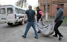 A communal worker and neighbors carry in a rug the body of a 38-year-old local resident who was killed when a missile exploded near his home in a residential area of Kharkiv on 15 April 2022.