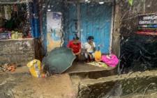 People are seen from inside a vehicle window as they sit by a closed shop carrying an umbrella as it rains in Kurseong which is about 50km from Siliguri on 8 August 2021. (AFP)