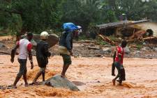 Residents walk through floodwaters past a damaged building in an area of Freetown on 14 August 2017 after landslides struck the capital of the west African state of Sierra Leone. Picture: AFP