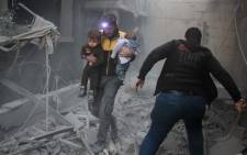 A Syrian man carries two children in the rubble of buildings following regime air strikes on the rebel-held besieged town of Douma in the eastern Ghouta region, on the outskirts of the capital Damascus, on 7 February 2018. Picture: AFP