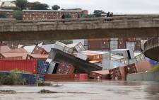 Residents of Umlazi township stand over a bridge and watch containers that fell over at a container storage facility following heavy rains and winds in Durban, on 12 April 2022. Picture: Phill Magakoe/AFP