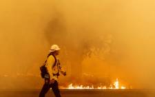 A Pacific Gas and Electric firefighter walks down a road as flames approach in Fairfield, California during the LNU Lightning Complex fire on 19 August 2020.  Picture: AFP