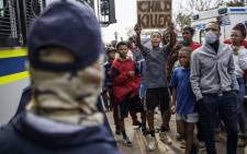 A resident holds a placard that reads "Child Killer" next to members of the South African Police Service (SAPS) outside the SAPS offices in Eldorado Park, near Johannesburg, on 27 August 2020, during a protest by community members after a 16-year old boy was allegedly shot dead by a police officer. Picture: AFP