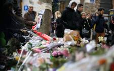 People spend a moment mourning the dead at the site of the attack at the Cafe Belle Equipe on rue de Charonne, prior to going to work early on 16 November 2015 in Paris, three days after the terrorist attacks that left over 130 dead and more than 350 injured. Picture: AFP.