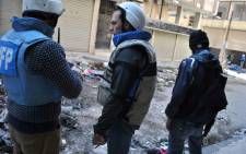 United Nations World Food Programme (WFP) workers stand near a rebel fighter in a street on February 8, 2014 on the second day of a humanitarian mission in a besieged district of the central city of Homs. Picture: AFP.