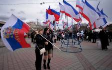 Two women hold a Russian flag next to a set of Crimean flags at Lenin Square in Simferopol on 16 March 2014 after Crimeans voted in a unique referendum on breaking away from Ukraine to join Russia. Picture: AFP.
