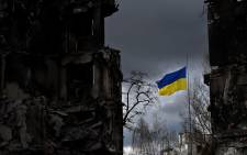FILE: The Ukrainian flag flutters between buildings destroyed in bombardment, in the Ukrainian town of Borodianka, in the Kyiv region on 17 April 2022. Picture: Sergei SUPINSKY/AFP