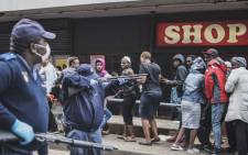 A South African policeman points his pump rifle to disperse a crowd of shoppers in Yeoville, Johannesburg, on 28 March 2020 while trying to enforce a safety distance outside a supermarket amid concern of the spread of COVID-19 coronavirus. Picture: AFP