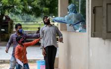 Residents hold a man as a health worker collects a swab sample from him to test for the COVID-19 coronavirus at a community gym centre on the outskirts of Hyderabad, India, on 8 October 2020. Picture: AFP.