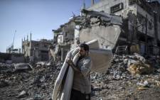 A Palestinian carries mattresses he found in the rubble of destroyed buildings on 27 July 2014 in the Shejaiya residential district of Gaza City. Picture: AFP.