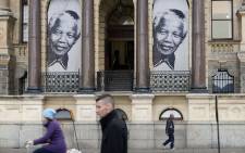 People walk past a banner with two pictures of Nelson Mandela as it hangs on the outside of the City Hall in 2013. Picture: AFP.