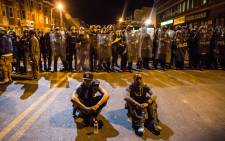 Two protesters sit on the ground in front of riot police minutes before a mandatory, city-wide curfew of 10 pm near the CVS pharmacy that was set on fire during rioting after the funeral of Freddie Gray, on 28 April, 2015 in Baltimore, Maryland. Picture: AFP.
