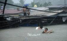 Residents try to cross through floodwaters as others wait on the roofs of their houses after a river overflowed in Manila. Picture: AFP.