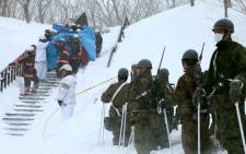 Firefighters carry a survivor rescued from the site of an avalanche in Nasu town, Tochigi prefecture, on 27 March, 2017, while Self Defense Force personnel look on. Picture: AFP.