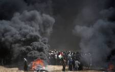 FILE; A Palestinian holds his national flag in the smoke billowing from burning tyres during clashes with Israeli forces near the border between the Gaza strip and Israel east of Gaza City on 14 May 2018. Picture: AFP.