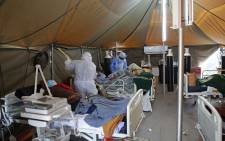 FILE: A professional healthcare worker wearing personal protective equipment (PPE) treats a patient in a tent dedicated to the treatment of possible COVID-19 coronavirus patients, while another cleans the ward at the Tshwane District Hospital in Pretoria on 10 July 2020. Picture: AFP
