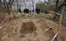 Media representatives and bystanders gather beside the bodies of a family after they were exhumed from a shallow grave in village of Havronshchyna, Kyiv region on April 10, 2022. Picture: Sergei Chuzavkov / AFP.