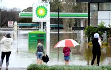People stand next to a flooded petrol station due to torrential rain in the Camden suburb of Sydney on 3 July 2022. Picture: Muhammad FAROOQ/AFP