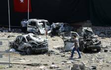 Turkish rescue workers stand by the wreckage of a vehicle as a police officer inspects a destroyed car and a man walks among the remains at the blast scene following a car bomb attack on a police station in the eastern Turkish city of Elazig, on 18 August 2016. Picture: AFP.