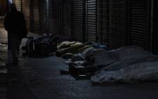 FILE: A man walks past homeless people sleeping outside a shop. Picture: EWN