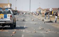 Stones are strewn along a main street as people gather outside the Tembisa Customer Care Centre after protesters set it on fire after a night of riots caused by angry community members demanding better service delivery in Tembisa on 1 August 2022. Picture: GUILLEM SARTORIO/AFP