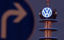 A street sign can be seen in front of the illuminated logo of German car maker Volkswagen (VW) on 10 December, 2015 in Hanover, central Germany. Picture: AFP.