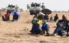 Striking Lonmin workers await news from the leaders, as police keep a close watch nearby. Picture: Taurai Maduna/EWN.