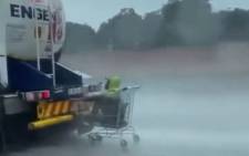 A screengrab of a man in a shopping trolley hitching a ride behind a fuel tanker in the rain outside Pretoria.