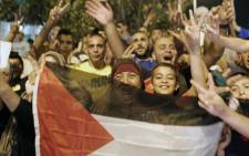 FILE: Palestinians flash the sign of victory wave a national flag as they celebrate in the streets in East Jerusalem the long-term truce agreed between Israel and the Palestinians on August 26, 2014