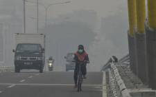 A cyclist makes her way across a bridge amid choking smog due to forest fires in Pekanbaru, Riau on 19 September 2019. Picture: AFP